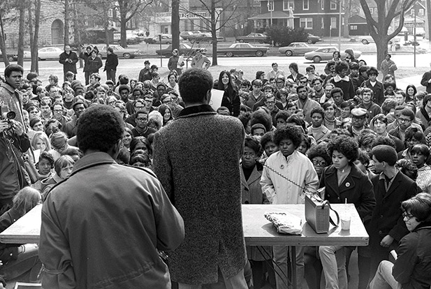 A black and white photograph of a man addressing a group of protestors