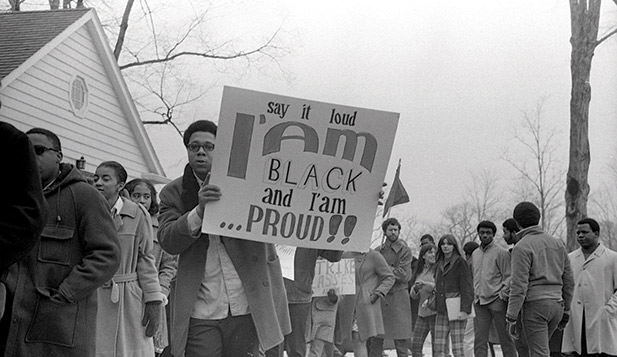 A black and white photograph of an African American man holding a sign which states I am Black and I am Proud!! 