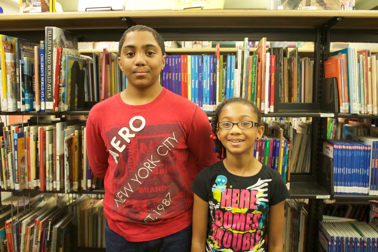 Aaron and Tia smile at the camera and stand in front of a bookshelf full of books.