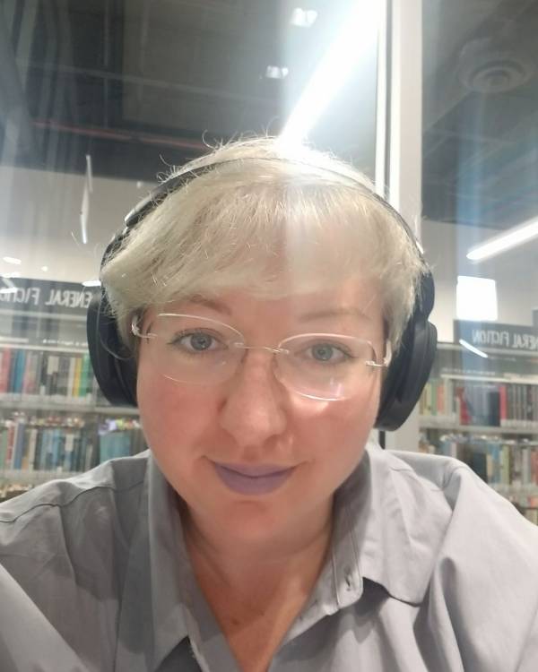 A smiling person wearing headphones and glasses