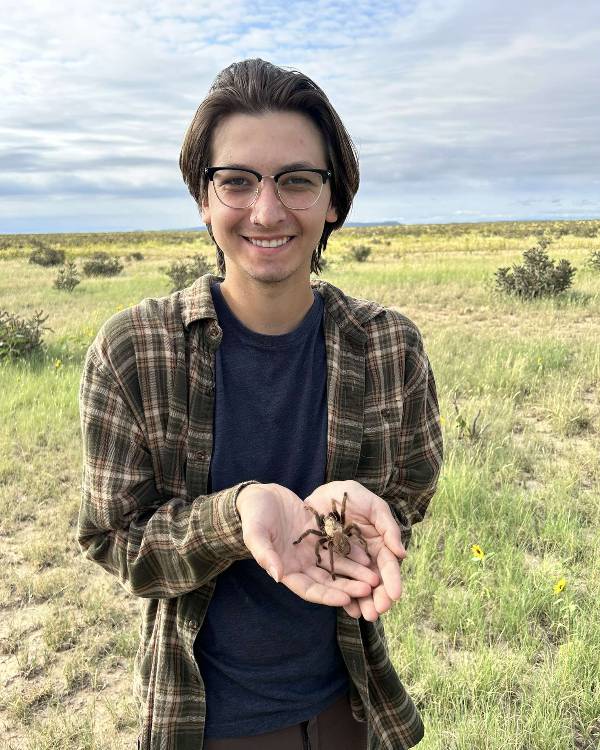 Smiling person outside holding a large spider