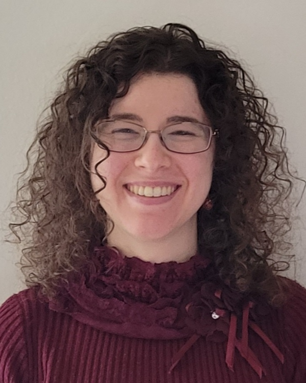 Smiling person with curly hair and glasses