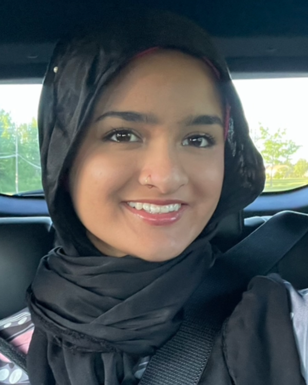 A selfie of a smiling person sitting in a car wearing a hijab and nose ring.