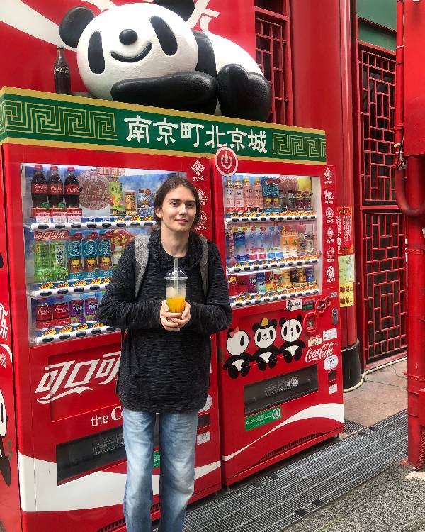 Smiling person standing in front of a vending machine holding a beverage