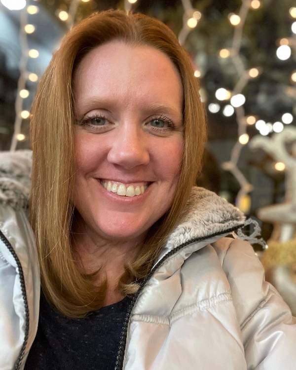 Smiling person with shoulder length red hair wearing a winter coat.