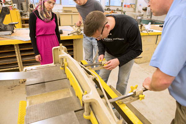One female and two male students work in the shop with a male professor.