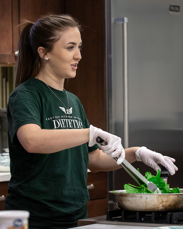 A female dietetics student tosses spinach in the demo kitchen.