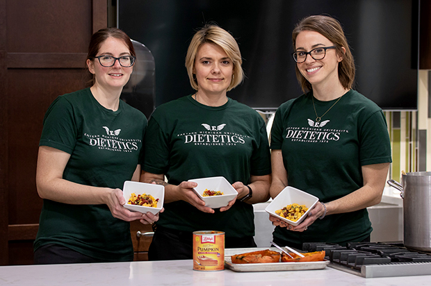 Three female dietetics students holding up food.