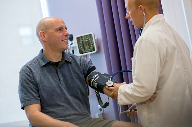 A student prepares to take a smiling man's blood pressure.