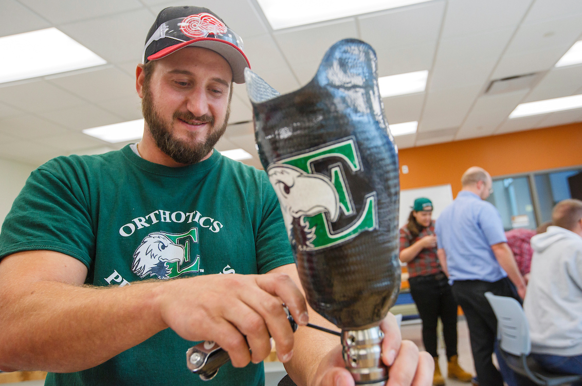 A student in EMU green works on a prosthetic leg with the EMU eagle logo on it.