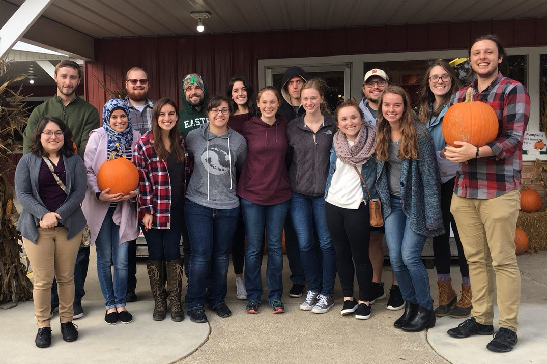 A group of students stand outside holding pumpkins.