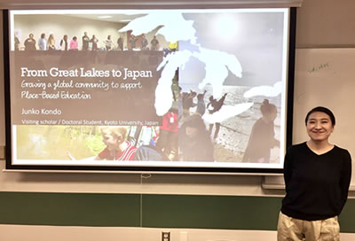 A photo of Junko Kondo standing next to her presentation.
