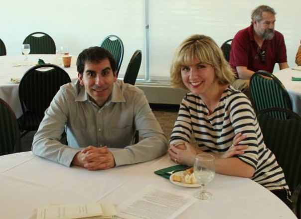 A man and a woman sit at a table eating and smiling.