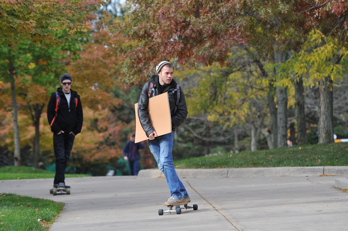 Two male students skateboarding on campus