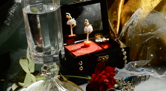 Feminine items are strewn across a table, includig a balerina music box, lace veil and a rose.