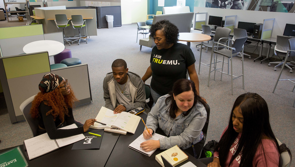 Image of a group of students working at a table with a faculty member offering guidance.