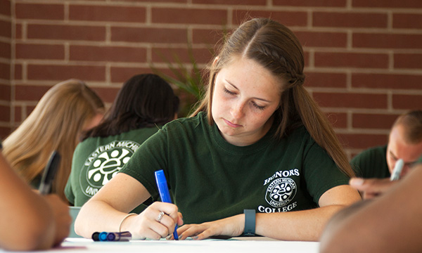 Girl with blond hair and green shirt writing in her notebook