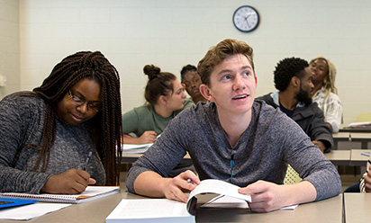 female student writing in notebook while male student is looking up in a classroom setting