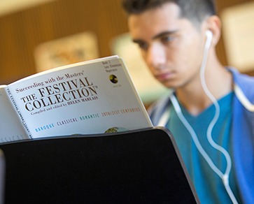 A student wearing in-ear headphones looks at a music book.