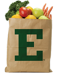 A brown paper bag with a green "E" on the side with fresh produce sticking out the top of the bag.