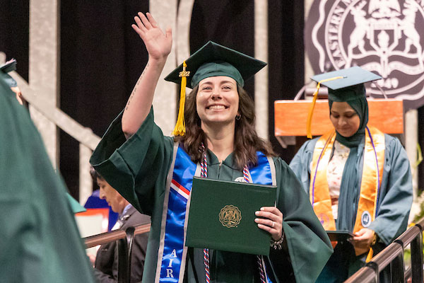 A photo of a EMU graduate waving after receiving her diploma.