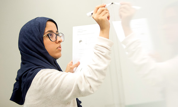 A photo of a female student writing on a white board.